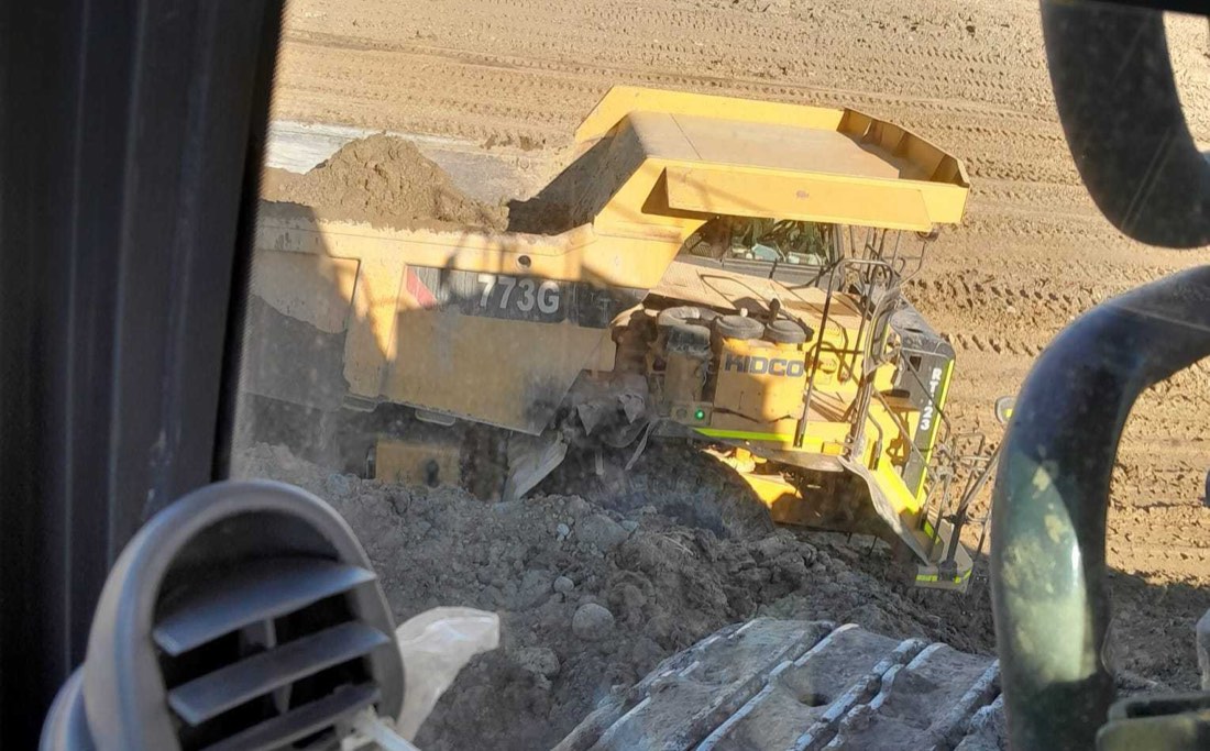 Track-type dozer pushing a windrow of fill across a subdivision pad with new homes on the skyline
