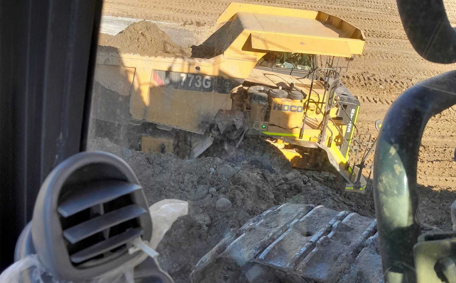 Track-type bulldozer pushing a windrow of earth across a graded pad on an active central Alberta site